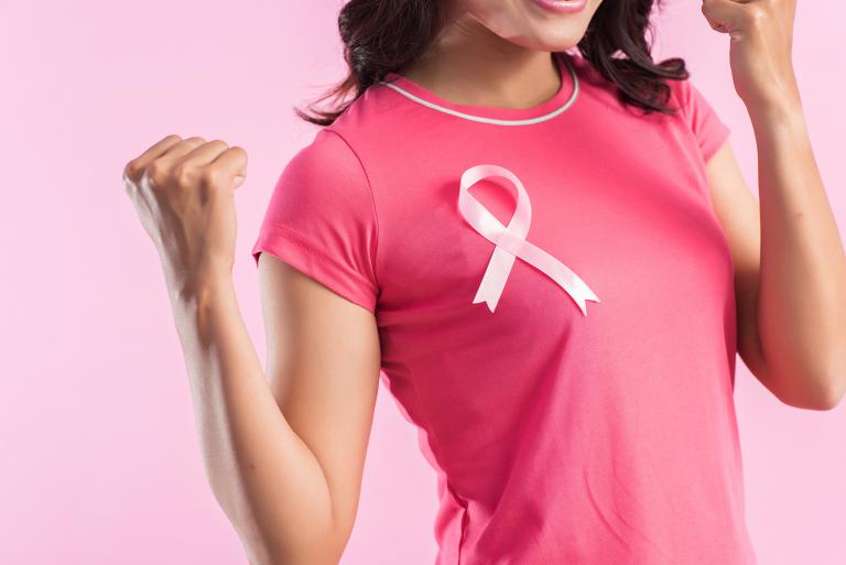 A woman wearing a breast cancer ribbon and flexing her muscles