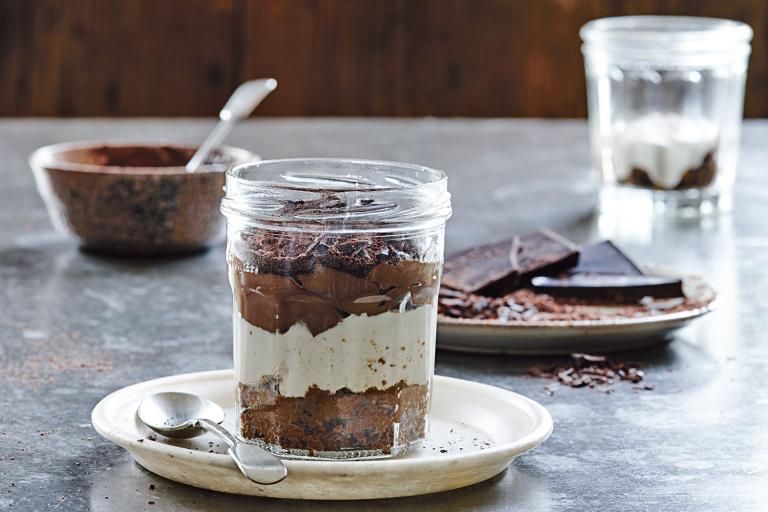 Tiramisu in a clear jar on a white plate with spoon. 